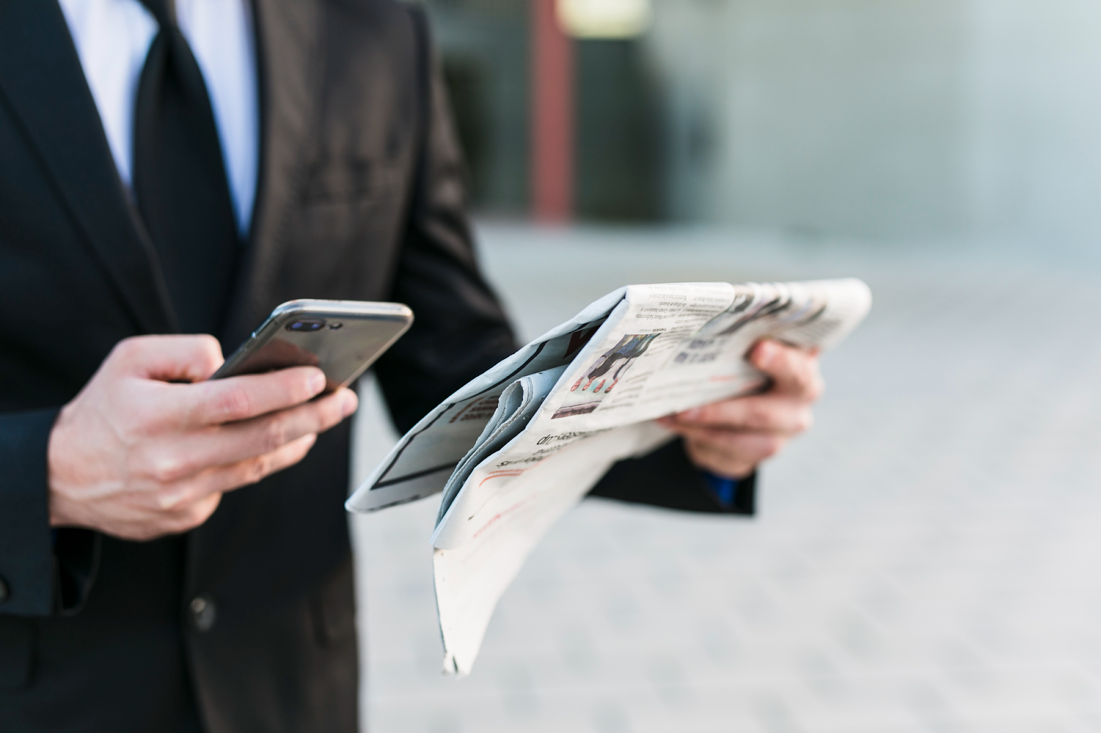 A businessman in a suit holding a smartphone in one hand and a newspaper in the other, demonstrating how a press release gains traction across both digital and print media.